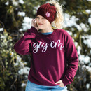 Woman standing in front of a snowy shrub wearing the Texas A&M Aggies Gig 'Em Scripty crewneck. Woman standing in front of a snowy shrub wearing the Texas A&M Aggies Gig 'Em Scripty crewneck.