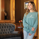 Woman in Stella Hotel leaning against a wall while wearing the embroidered crewneck.