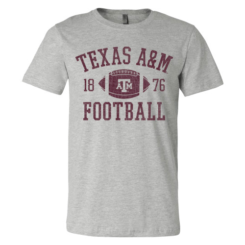 Heather gray Texas A&M Football T-shirt featuring arched maroon lettering, an A&M football graphic, and 1876 accents across the chest. Classic game day tee celebrating Texas A&M football tradition.
