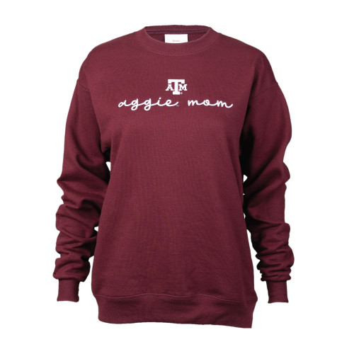 Maroon crewneck sweatshirt with an ATM logo centered above script font aggie mom all embroidered in white.