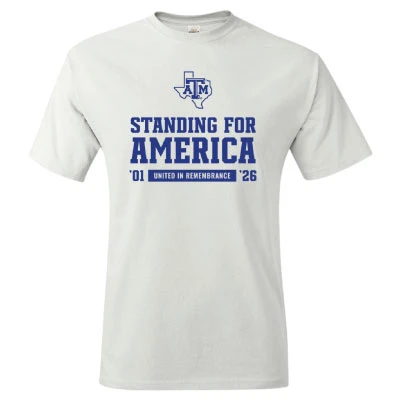 white Texas A&M T-shirt featuring a Texas A&M logo, bold “Standing for America” lettering, ’01 and ’26 dates, and “United in Remembrance” text on the front.