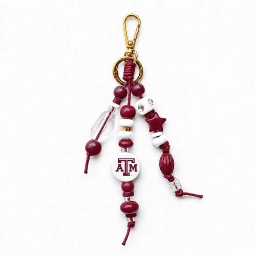 Texas A&M bag charm featuring maroon, white, clear, and gold-tone beads, a round white A&M logo bead, maroon star accent, decorative strands, and gold-tone clip hardware.