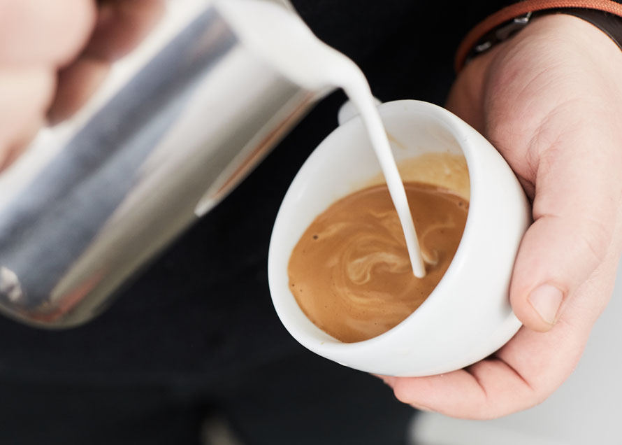 Pouring milk from a steaming pitcher high above a cup