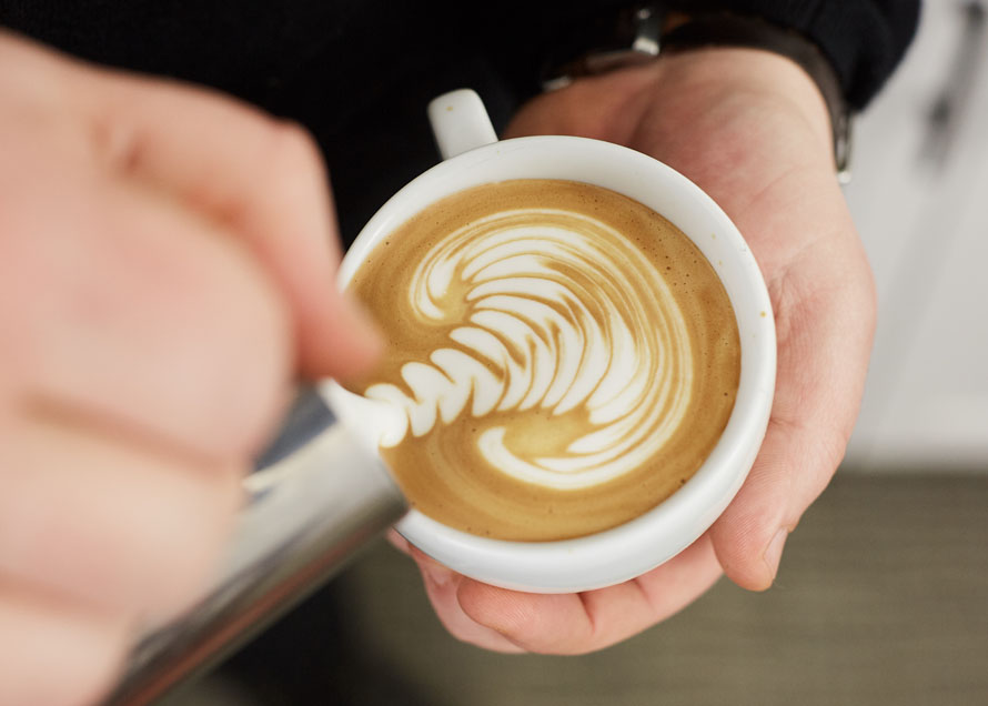 Waves in latte art stacked to the top of the cup, ready to be Cut through to finish the design