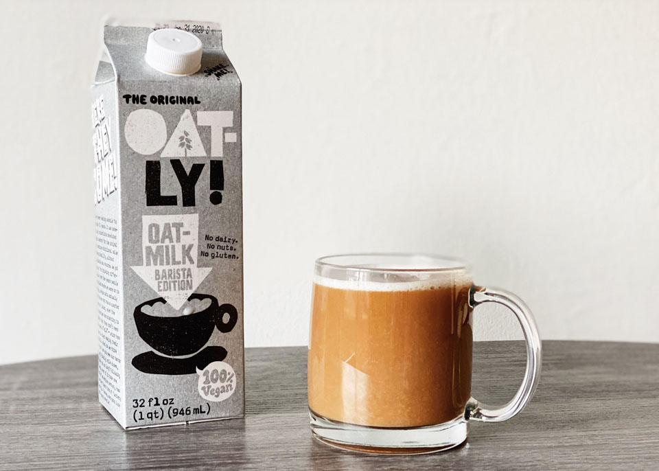 Carton of Oatly next to a mug of milky coffee