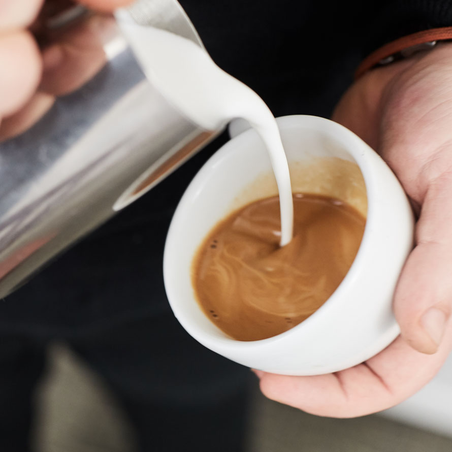 Pouring milk from high above the coffee to mix the two together