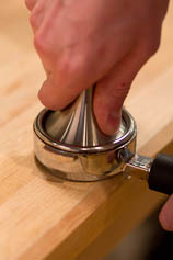 Tamp your coffee dose firmly, aiming to be as even as possible with your tamper. Tamping ground coffee into a portafilter.