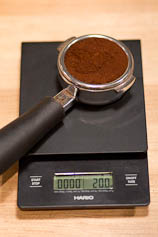 Weigh your espresso dose before brewing. Portafilter with ground coffee on a scale.