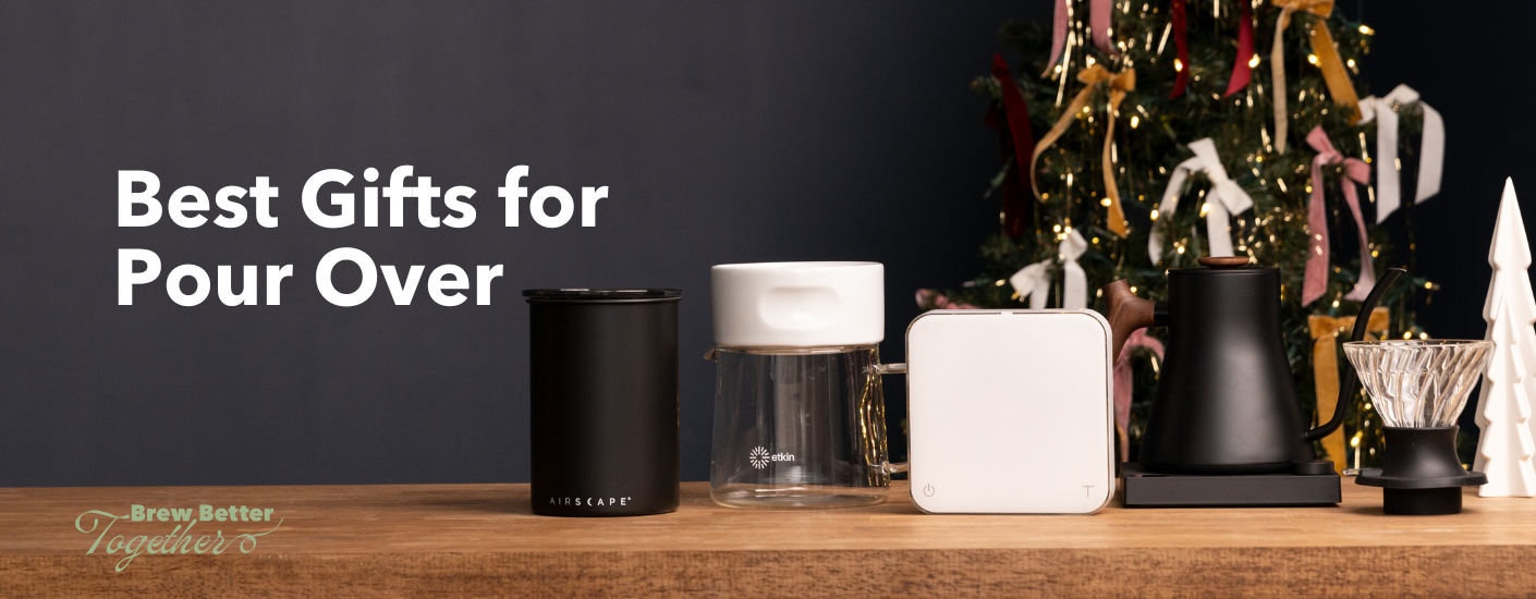 A coffee storage canister, Etkin brewer and server, Acaia Pearl scale, and black EKG Stagg Kettle sitting on a table with holiday decorations.