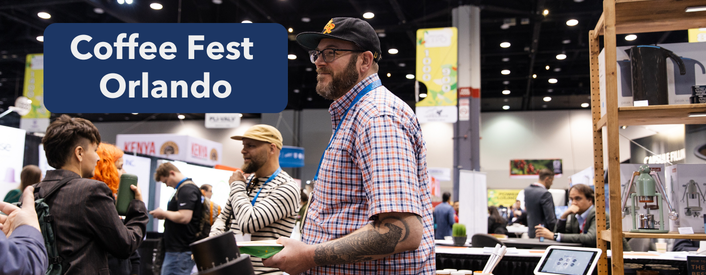 Man in a baseball cap smiling at a customer at a booth at a trade show.