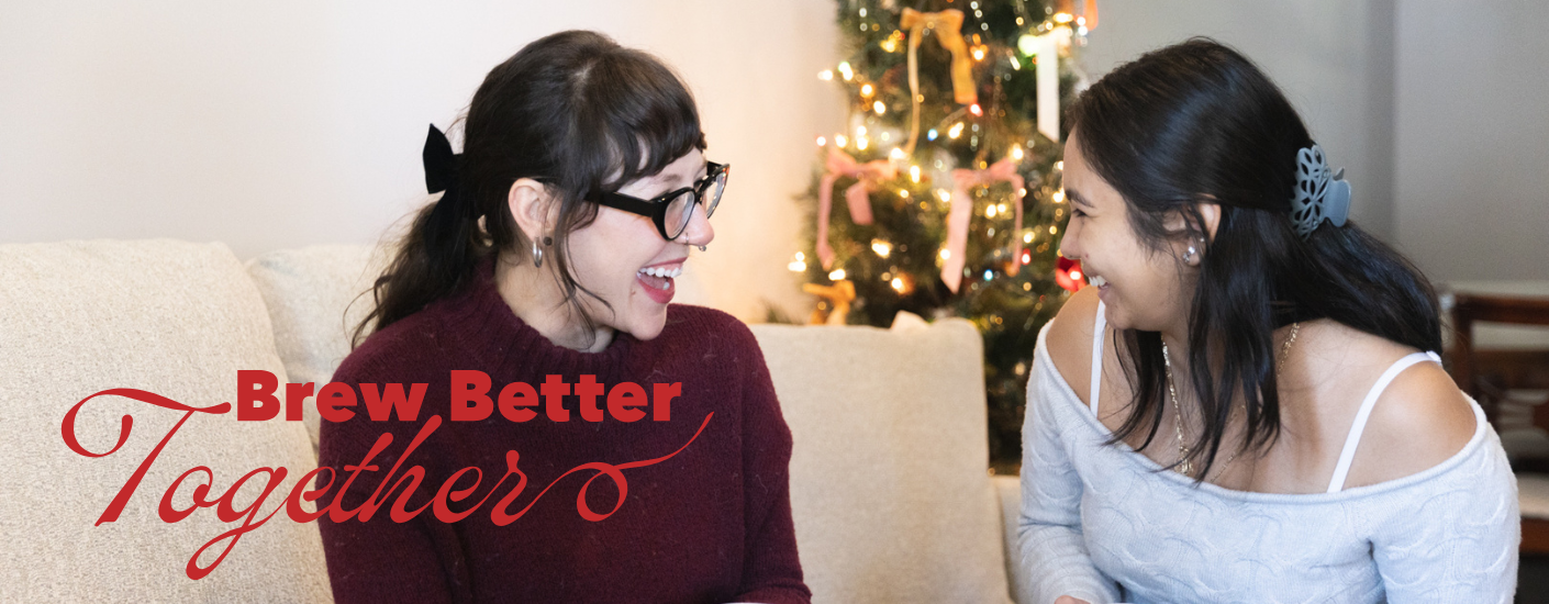 Two women sitting on a couch laughing with a Christmas tree in the background