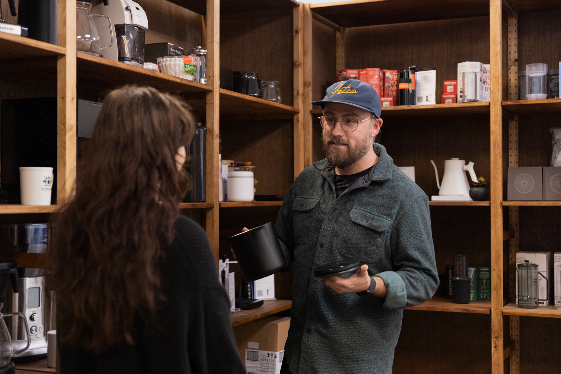 Man holding a carafe for the Fellow Aiden talking to a woman about it in a retail space.