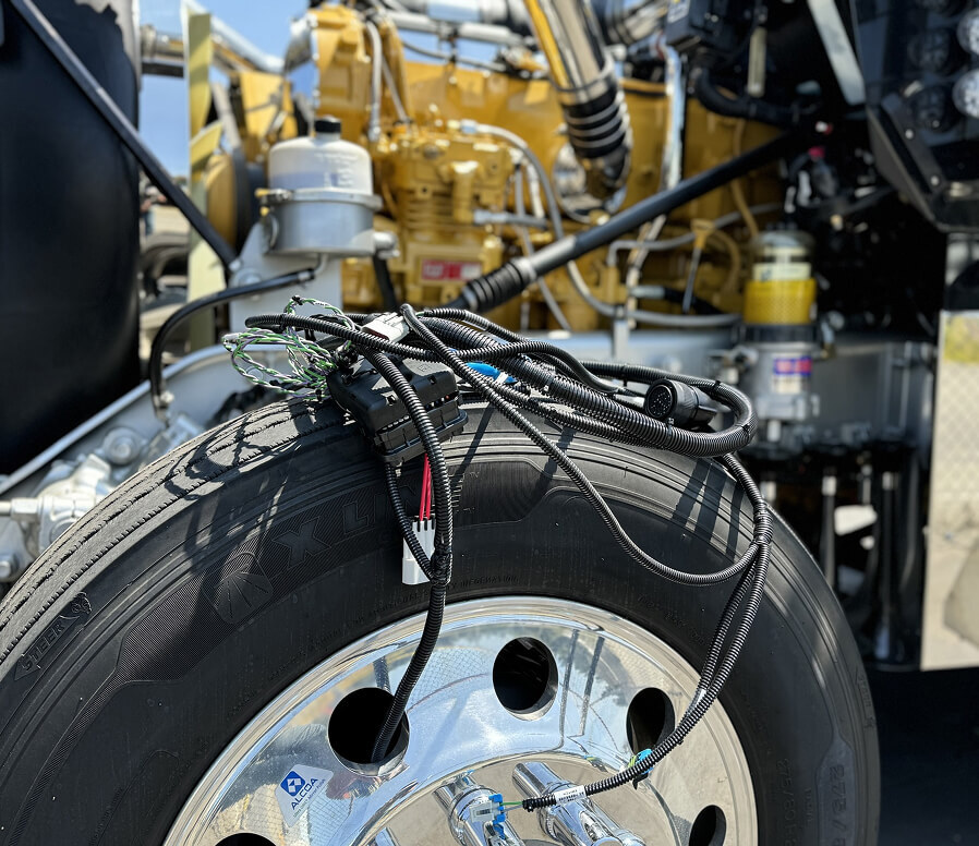 Engine wiring harness laid across truck tire with CAT engine visible during conversion