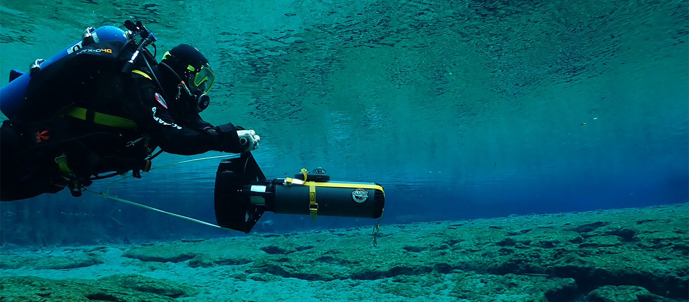 Underwater a scuba diver is seen on the left, holding a DPV console with our console gauge mount attached.