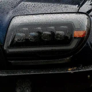 Close-up of an AlphaRex headlight on a black 4Runner covered in raindrops