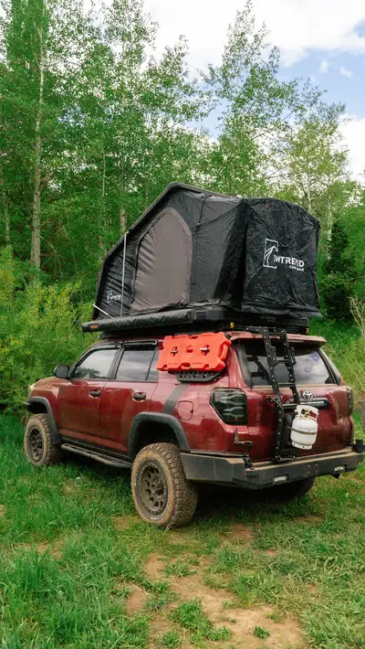 Red 4Runner with a rooftop tent parked in a green aspen meadow