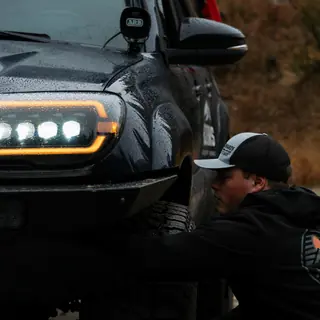 AlphaRex LED headlight lit up on a black 4Runner while a man kneels by the front wheel