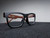 Chunky matte-black square eyeglass frames with wood-finish temples on dark felt
