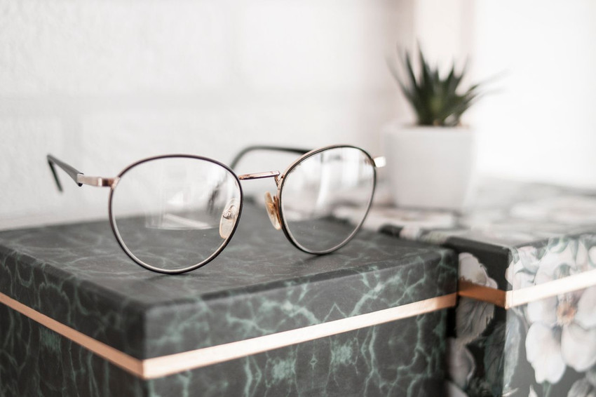 Round gold wire-rim eyeglasses resting on a green marble box