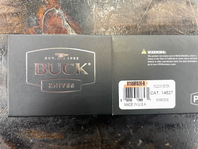 This Knife
Blade: Clip point blade with a hollow grind and satin finish made from MagnaCut steel.
Opener: Classic nail nick opener.
Handle: Ebony wood handle with nickel silver bolsters.
Lock: Famous Buck 110 lockback.
Carry: Tip-up carry pocket clip for right side carry.
Buck Knives 110 Slim Elite Heritage
The Buck 110 Slim Elite Heritage keeps everything that made the original 110 a legend—and trims the fat where it counts. You still get the unmistakable clip point blade with a hollow grind, the time-tested nail nick opener, and Buck’s rock-solid lockback mechanism. The difference? A slimmer, lighter profile and a serious steel upgrade to premium MagnaCut, delivering exceptional edge retention, toughness, and corrosion resistance without sacrificing tradition.

Think of it as the classic 110 after a few long miles in the backwoods and a little time at the gym. Same dependable soul, same proven design—just easier to carry and quicker to forget it’s in your pocket until you need it. It’s heritage you can feel good about carrying every day, built for the long haul just like its predecessors.

Overall Length: 8.63"
Blade Length: 3.75"
Blade Thickness: 0.12"
Blade Material: CPM MagnaCut
Blade Style: Clip Point
Blade Grind: Hollow
Finish: Satin
Edge Type: Plain
Handle Length: 4.88"
Handle Material: Wood
Color: Wood
Bolster Material: Nickel Silver
Weight: 5.40 oz.
User: Right Hand
Pocket Clip: Tip-Up
Knife Type: Manual
Opener: Nail Nick
Lock Type: Lockback
Brand: Buck Knives
Model: 110
Country of Origin: USA
Best Use: Camp/Hike, Hunting
Product Type: Knife