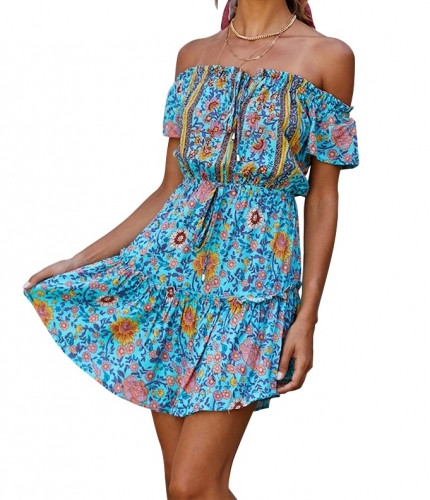Model wearing the Robyn Ryan™ Coastal Bloom Tropical Garden Midi Dress featuring a sky-blue base with vibrant tropical floral print in orange, mustard, pink, ivory, and deep teal accents. The midi-length silhouette flows naturally with a flattering tie-waist detail, styled for a resort and coastal vacation look.