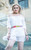 Candid motion shot of Hope in the White Swiss Dot Mini Dress, highlighting the flow of the sleeves, ruffle neckline detail, and natural movement of the fabric in an urban setting. Photography by Matt Vince.