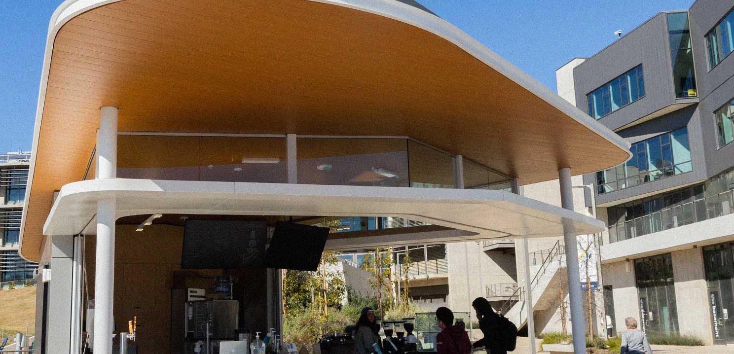 A small standalone open air building with a coffee shop inside showing a few people and coffee equipment.