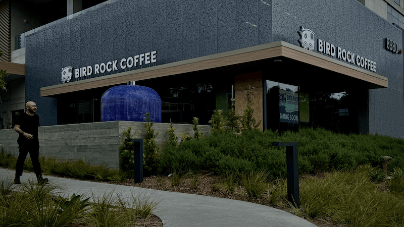 A modern exterior of the Bird Rock Village cafe with a person walking down a path.