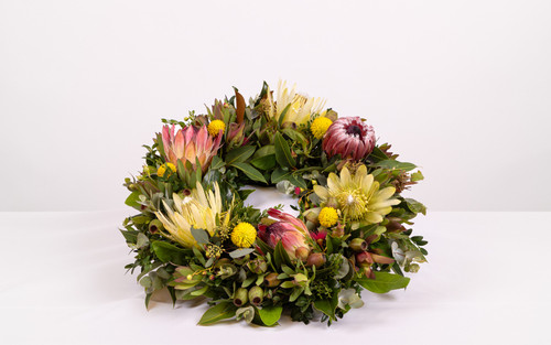 A 35cm wreath arrangement for displaying at a funeral, featuring native flowers such as protea, leaucadendron, wattle and billy button.