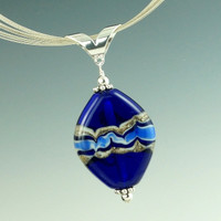 A beautiful base of deep cobalt blue with rich layers of ivory and blue glass with silver make this swirl pendant really pop. After shaping, the surface of one side is heated and then swirled with a thin rod of glass to create its own beautiful design, while the other side is left natural. Each each side offers its own distinct style.