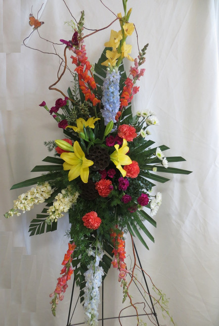 Heavenly Solace Funeral Standing Spray by Enchanted Florist Pasadena TX. Delivery of beautiful funeral flowers to local Houston and Pasadena funeral homes and churches. Same day funeral flower delivery. Yellow lilies, orange carnations, fragrant yellow stock. RM535