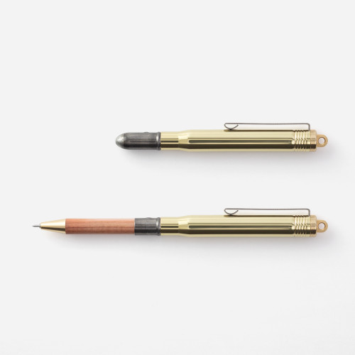 Traveler's Company BRASS Ballpoint Pen showing compact brass holder and raw iron clip next to packaging. / Stylo bille en laiton Traveler's Company BRASS présentant un corps compact en laiton brut et un clip en fer.