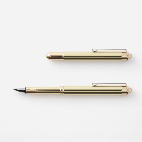 TRAVELER'S COMPANY TRC BRASS Fountain Pen in Solid Brass. A compact pocket pen showing its raw unplated brass cap, golden metal body, steel fine nib, and an industrial iron pocket clip. / Stylo-plume TRAVELER'S COMPANY TRC BRASS en laiton massif. Un stylo de poche compact présentant un capuchon en laiton brut, une plume fine en acier et un clip rétro au fini fer industriel.
