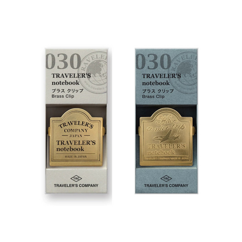 TRAVELER'S Notebook 030 Brass Clips. Two solid brass clips: one featuring a vintage airplane with "Have a nice trip" text, and the other with the TRAVELER'S COMPANY logo. Clips en laiton TRAVELER'S Notebook 030. Deux pinces en laiton massif : une avec un avion vintage et l'inscription "Have a nice trip", et l'autre avec le logo TRAVELER'S COMPANY.