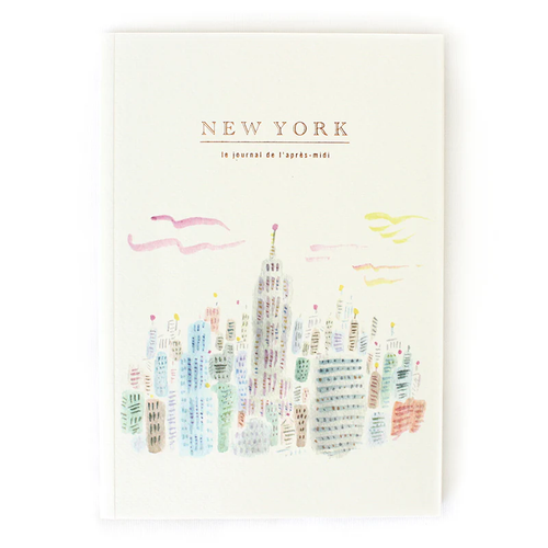 A5 travel journal featuring a dark blue watercolor illustration of the New York City skyline at night with gold stars and city lights on the cover. Carnet de voyage A5 avec une illustration à l'aquarelle bleu foncé de la skyline de New York la nuit, avec des étoiles dorées et des lumières de la ville sur la couverture.