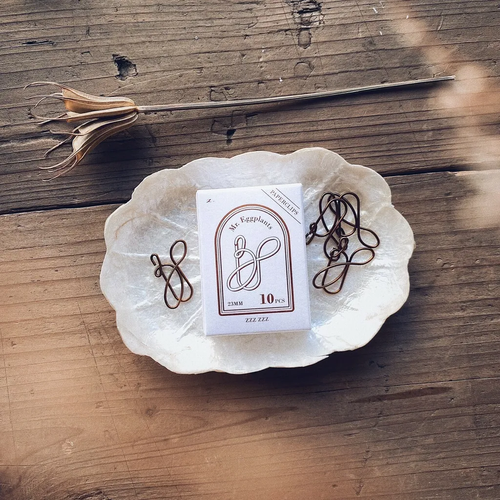 Mr. Eggplants Paperclip Z Set featuring 10 cursive Z-shaped metal clips in matte antique gold, presented in a white gold-foiled box. Lot de trombones Mr. Eggplants en forme de lettre Z cursive, en métal doré antique mat, présentés dans une boîte blanche avec dorure.