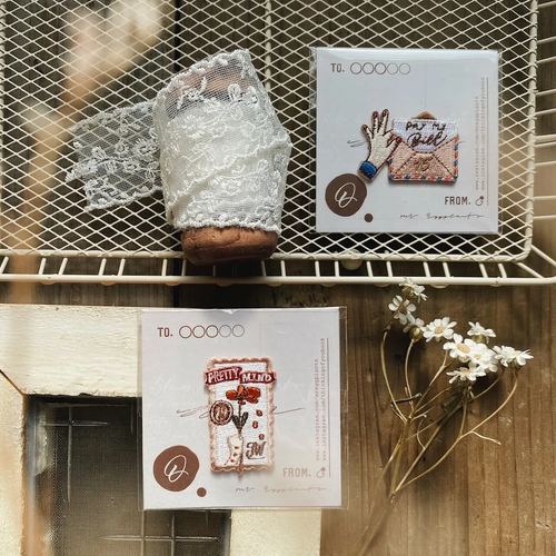 Mr. Eggplants Passing Notes Embroidery Sticker Patch featuring two designs: a vintage-style letter envelope and a postage stamp with detailed needlework. Écusson autocollant brodé Mr. Eggplants "Passing Notes" présentant deux modèles : une enveloppe de lettre vintage et un timbre-poste brodé.