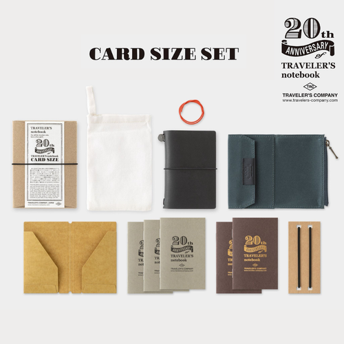 TRAVELER'S Notebook Card Size 20th Anniversary Set in Black. A miniature black leather notebook shown with its navy cotton zipper case, kraft folder, and five refills. Kit 20ème Anniversaire TRAVELER'S Notebook Taille Carte en Noir. Un carnet miniature en cuir noir avec sa pochette zippée en coton bleu marine, dossier kraft et cinq recharges.