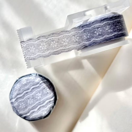 Pion Ribbon Washi Tape Grey Lace. A 1.5cm wide washi tape with shaped edges featuring an intricate illustrated grey lace pattern. Ruban adhésif Washi déco Pion Grey Lace (花灰). Un ruban de 1,5 cm aux bords découpés illustrant un motif de dentelle grise complexe.