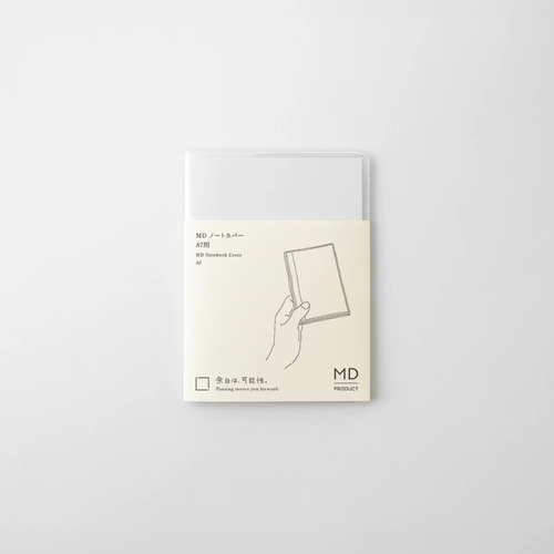 MIDORI MD Notebook Clear Cover A7 pocket size. A transparent, flexible plastic notebook sleeve featuring a built-in pen holder loop on the interior back flap, fitted over a mini cream notebook. / Protège-carnet transparent A7 de poche en PVC MIDORI MD Notebook. Une couverture plastique flexible transparente pour mini carnet dotée d'un passant pour stylo intégré sur le rabat intérieur arrière.