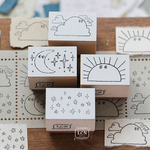 Lin Chia Ning "Weather" Rubber Stamp Set. A set of four wooden-backed stamps featuring a sun, clouds, moon with stars, and a star cluster. Set de tampons en caoutchouc Lin Chia Ning "Météo". Un lot de quatre tampons en bois représentant un soleil, des nuages, une lune avec des étoiles et un amas d'étoiles.