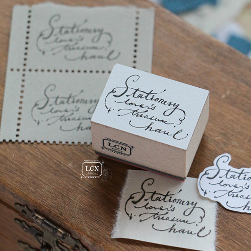 Lin Chia Ning "Treasure Haul" Rubber Stamp. A vintage-style stamp depicting a collection of stationery treasures, mounted on a wooden block. Tampon en caoutchouc Lin Chia Ning "Trésors de Papeterie". Un tampon de style vintage représentant une collection de papeterie, monté sur un bloc en bois.