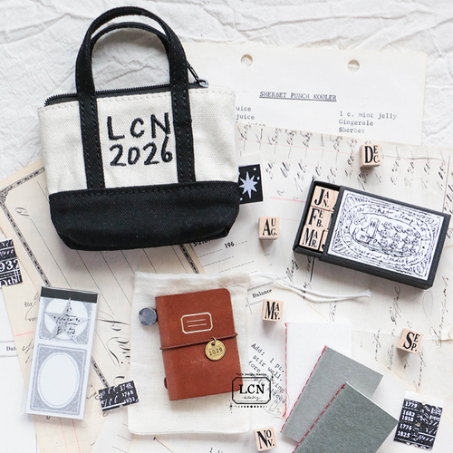 Lin Chia Ning 2026 Mini Tote Stationery Set with a brown leather mini notebook, moon brass charm, and black sticker roll. Coffret de papeterie Lin Chia Ning 2026 avec un mini carnet en cuir marron, une breloque lune en laiton et un rouleau d'autocollants noirs.