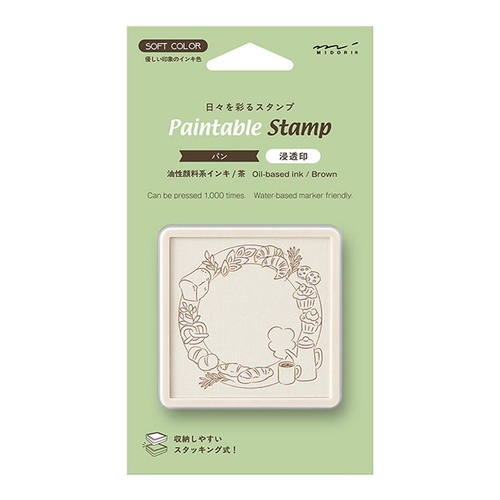 Midori pre-inked paintable stamp Bread theme in a brown square body. Shows a soft brown ink frame pattern with hand-drawn bakery motifs designed by Sayo Koizumi. / Tampon auto-encreur à peindre Midori thème Pain, boîtier carré marron. Montre un motif de cadre à l'encre marron clair avec des motifs de boulangerie conçus par Sayo Koizumi.