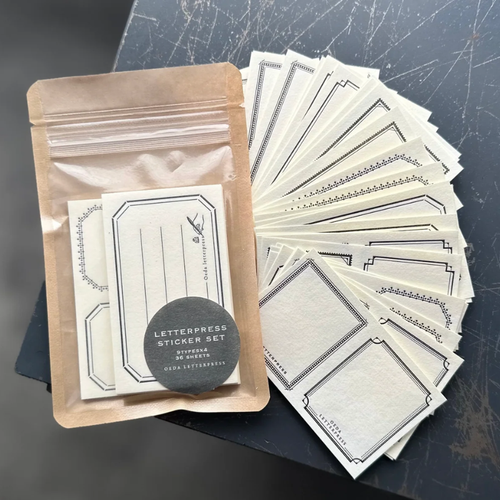 OEDA LETTERPRESS Sticker Set in Black showing textured white business card sized paper stickers with black letterpress frames. / Ensemble d'autocollants OEDA LETTERPRESS en Noir présentant des autocollants en papier blanc texturé format carte de visite imprimés en typographie noire.