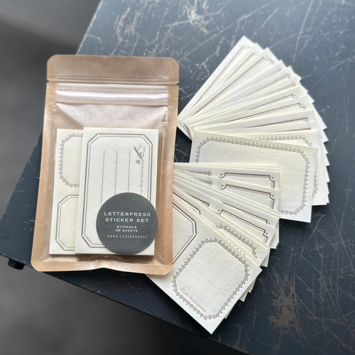 OEDA LETTERPRESS Sticker Set in Bronze showing textured white business card sized paper stickers with bronze metallic letterpress frames. / Ensemble d'autocollants OEDA LETTERPRESS en Bronze présentant des autocollants en papier blanc texturé format carte de visite imprimés en typographie bronze métallique.