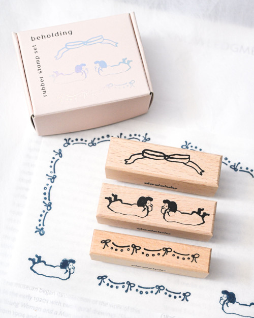 dodolulu Rubber Stamp Set Beholding three-piece beech wood stamp set featuring two girls, a ribbon, and knot motifs. / Ensemble de tampons en caoutchouc dodolulu Beholding comprenant trois tampons en bois de hêtre avec deux filles, un ruban et des motifs de nœuds.