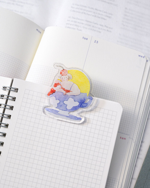 dodolulu Journaling Clip Afternoon Tea acrylic memo clip with café illustrations holding photos and notes on a desk. / Pince-mémo en acrylique dodolulu Journaling Clip Afternoon Tea avec illustrations de café pour exposer des photos et des notes sur un bureau.