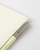 MIDORI MD Notebook Clear Cover B6 Slim edition. A transparent, flexible plastic notebook sleeve featuring a built-in pen loop on the interior back flap, fitted over a minimalist cream notebook. / Protège-carnet transparent B6 Slim en PVC MIDORI MD Notebook. Une couverture plastique flexible transparente dotée d'un passant pour stylo intégré sur le rabat intérieur arrière.