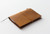TRAVELER'S Notebook Starter Kit Passport Size in Camel. A rustic camel leather cover with a blank notebook refill, green spare elastic, and a cotton bag. Kit de démarrage TRAVELER'S Notebook Taille Passeport en Camel. Une couverture en cuir camel rustique avec une recharge de carnet vierge et un élastique de rechange vert.